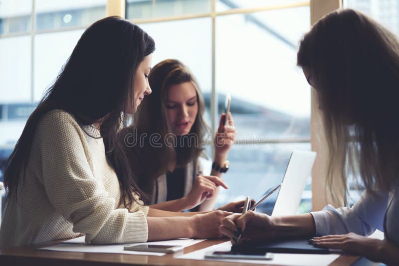 Roupa de desenhistas das meninas que trabalha junto no café usando laptop e na aplicação para a modelagem da Web usando o wifi foto de stock royalty free Roupa de desenhistas das meninas que trabalha junto no café usando laptop e na aplicação para a modelagem da Web usando o wifi foto de stock royalty free