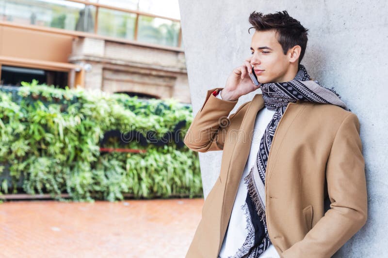 Roupa vestindo do inverno do homem novo na rua usando seu telefone Indivíduo novo com penteado moderno com revestimento, calças d fotos de stock royalty free Roupa vestindo do inverno do homem novo na rua usando seu telefone Indivíduo novo com penteado moderno com revestimento, calças d fotos de stock royalty free