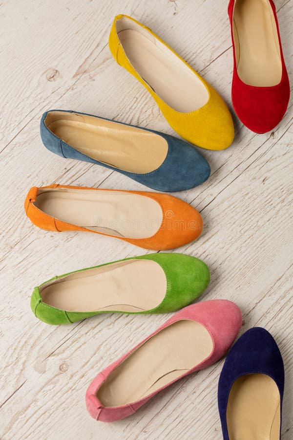 Row of colorful shoes ballerinas on a white wooden background.