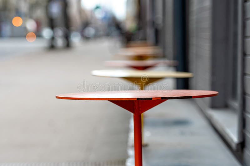 Row with empty street cafe tables on defocused city background, pandemic constraints concept