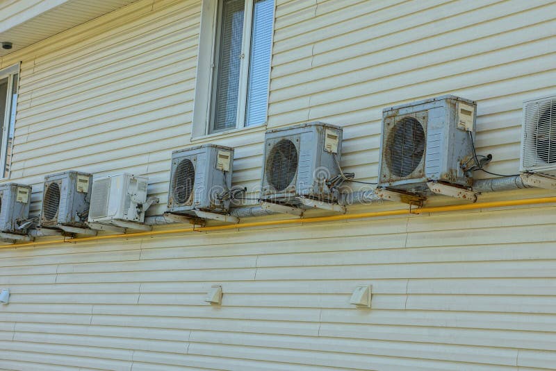 A row of gray air conditioners on a brown wall of a building with a window