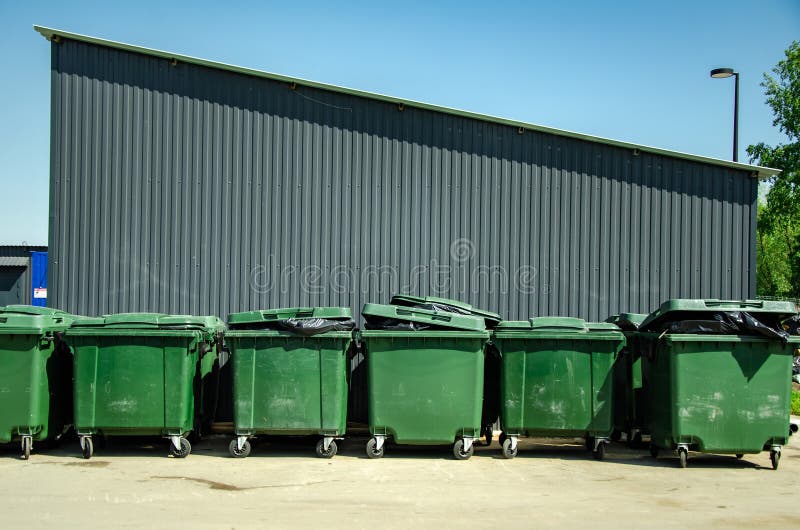 Row of Green Trash Bins Against a Warehouse Wall stock photography