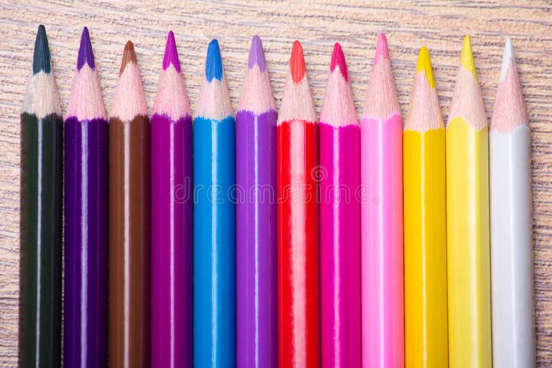 Row of many colored drawing pencils on wooden table