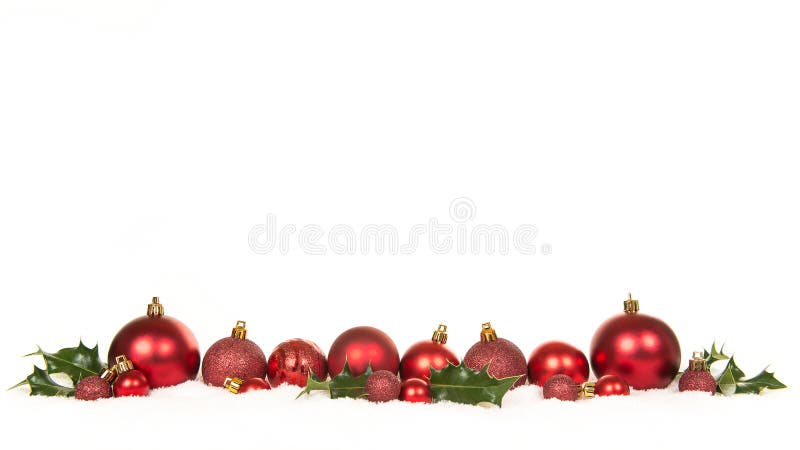 Row of red christmas ball decorations and green holly ilex in the snow