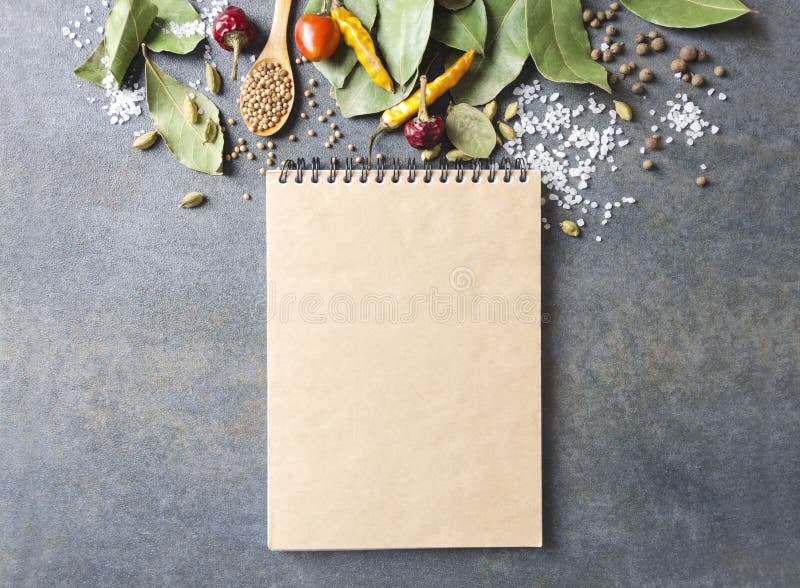 Top view of blank cookbook and lot of spieces and herbs on grey kitchen table.Empty space for your text and design