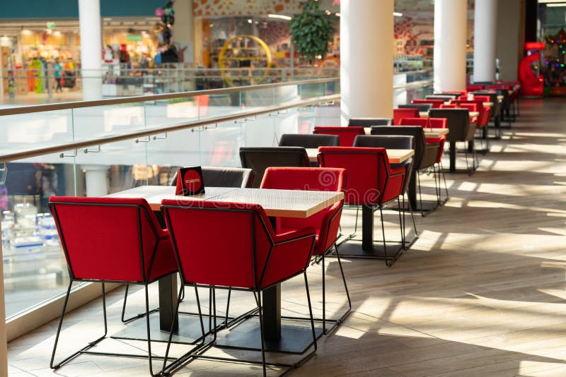 A row of tables with soft chairs for visitors to the food court of a modern shopping center