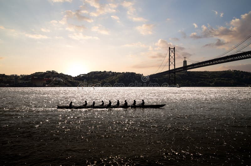 Silhouette of people on rowing boat on the sea with suspension bridge in the background at sunset. Lisbon, Portugal. Silhouette of people on rowing boat on the sea with suspension bridge in the background at sunset. Lisbon, Portugal.