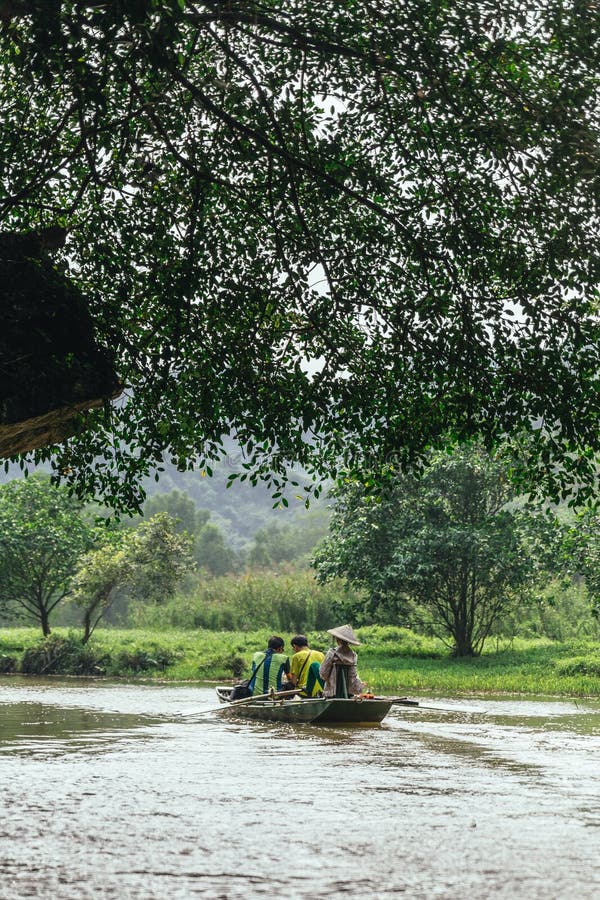 Rowing woman row a boat with tourist on the river under branches of trees at Trang An Grottoes in Ninh Binh, Vietnam stock photo Rowing woman row a boat with tourist on the river under branches of trees at Trang An Grottoes in Ninh Binh, Vietnam stock photo