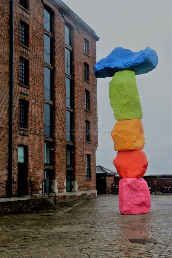 Liverpool, England – July 27, 2019: Historic brickstone warehouse, part of the Royal Albert Dock, and modern, colorful sculpture called Liverpool Mountain, installed in 2018. Artist: Ugo Rondinone.  Europe. Liverpool, England – July 27, 2019: Historic brickstone warehouse, part of the Royal Albert Dock, and modern, colorful sculpture called Liverpool Mountain, installed in 2018. Artist: Ugo Rondinone.  Europe.