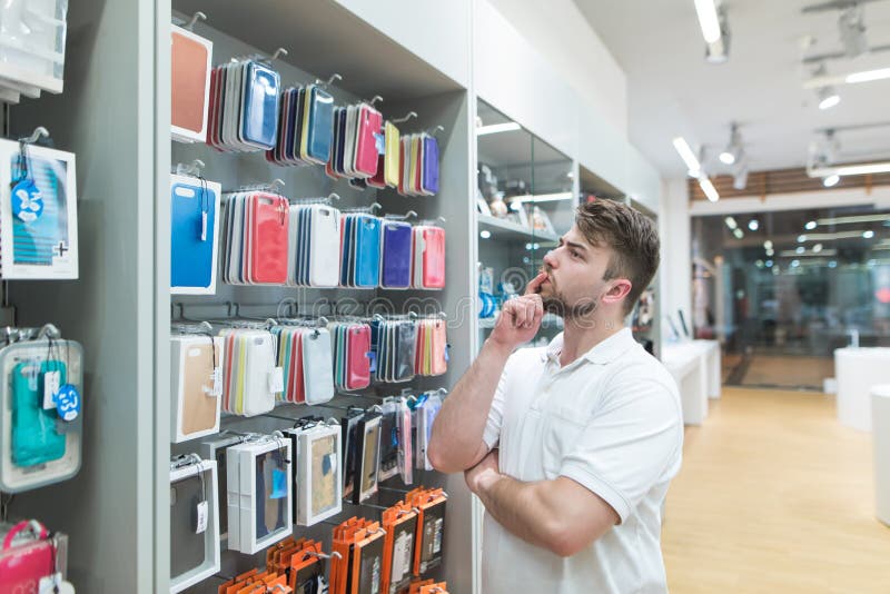 Rozważny mężczyzna wybiera skrzynki dla smartphone w akcesoriach wydziałowych przy nowożytnym elektronika sklepem zdjęcie stock Rozważny mężczyzna wybiera skrzynki dla smartphone w akcesoriach wydziałowych przy nowożytnym elektronika sklepem zdjęcie stock