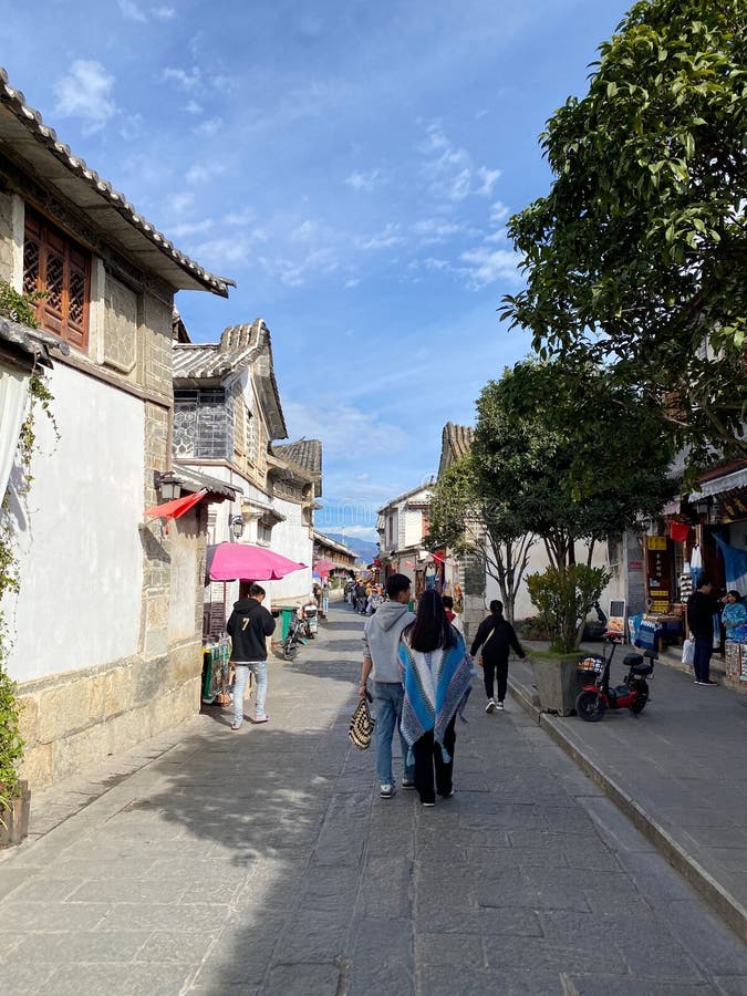 Rua arrebentada numa cidade antiga com arquitetura e turistas andando sob um céu azul claro foto de stock