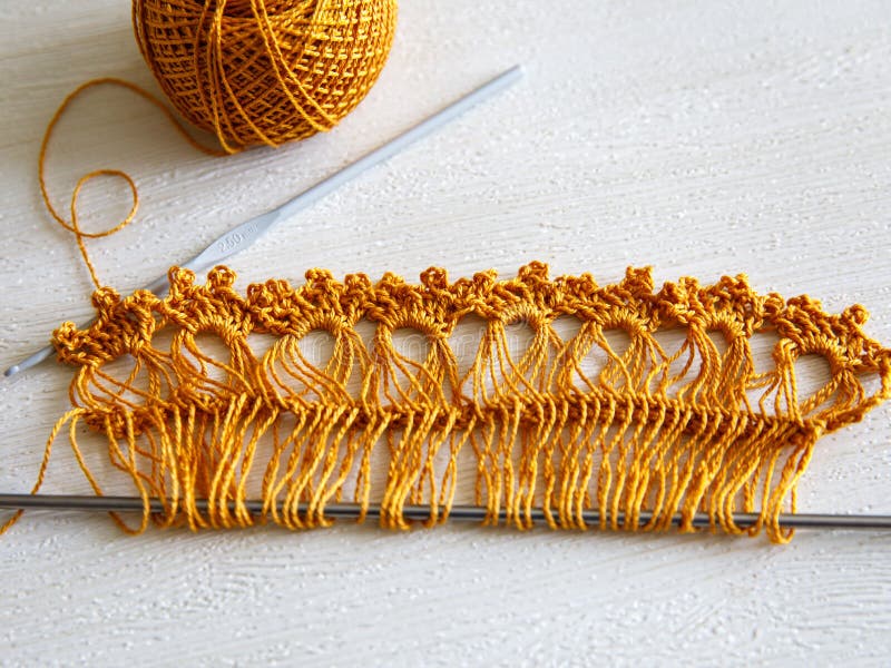 Ribbon for making lace on Adjustable crochet fork, crocheting hook and yellow brown golden cotton yarn ball on white wooden background, top veiw flat lay. Step by step, step 2, process of making lace. Ribbon for making lace on Adjustable crochet fork, crocheting hook and yellow brown golden cotton yarn ball on white wooden background, top veiw flat lay. Step by step, step 2, process of making lace