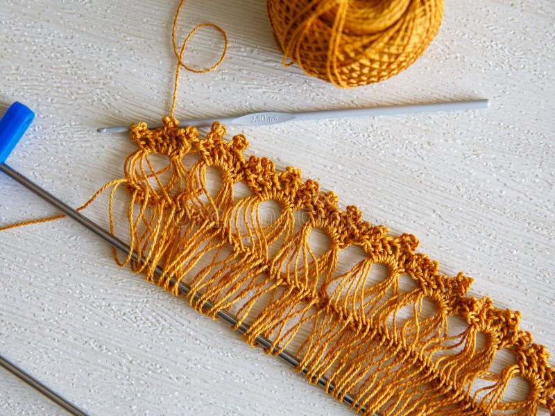 Ribbon for making lace on Adjustable crochet fork, crocheting hook and yellow brown golden cotton yarn ball on white wooden background, top veiw flat lay. Step by step, step 2, process of making lace. Ribbon for making lace on Adjustable crochet fork, crocheting hook and yellow brown golden cotton yarn ball on white wooden background, top veiw flat lay. Step by step, step 2, process of making lace