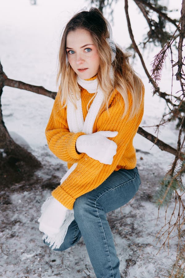 Rubia adolescente en un suéter amarillo afuera en invierno. una adolescente caminando con ropa de invierno en un bosque nevado fotos de archivo libres de regalías
