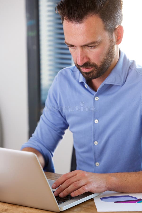 Ruchliwie dorośleć mężczyzna pracuje na laptopie przy jego biurkiem