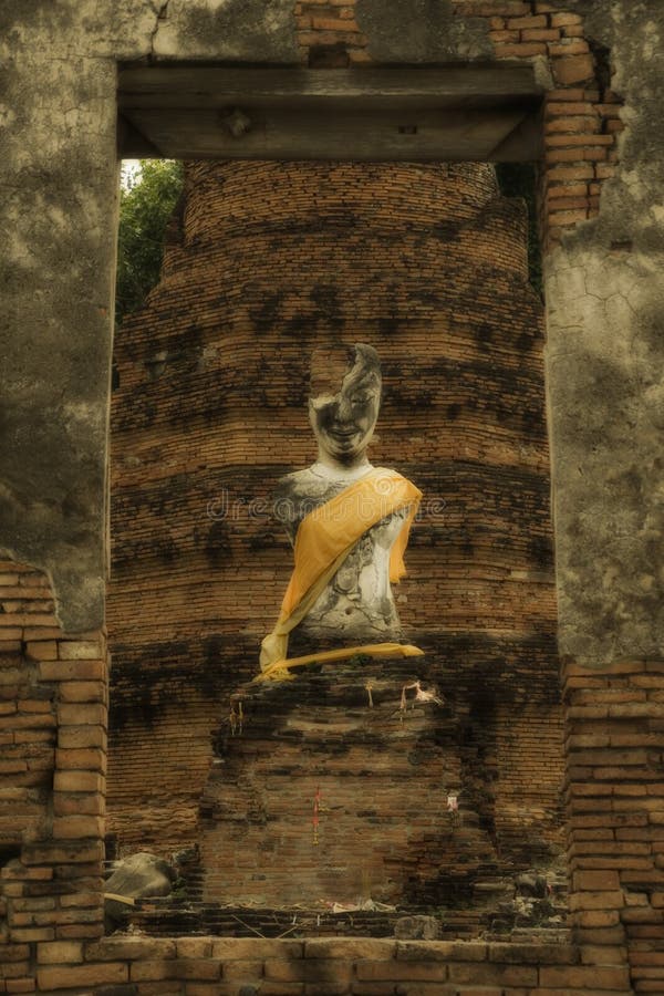 Ruin buddha statue of wat Suwandawas, Ayutthaya. The ancient abandoned ruin statue of Buddha locate in middle of the city of Ayutthaya. This collapse temple is one among hundreds of Wat spread out all over the province. The monument surface cracked reveal local red-brick inside. The sculpture has no arms and only half face with yellow dressing decorated by faithful villager.