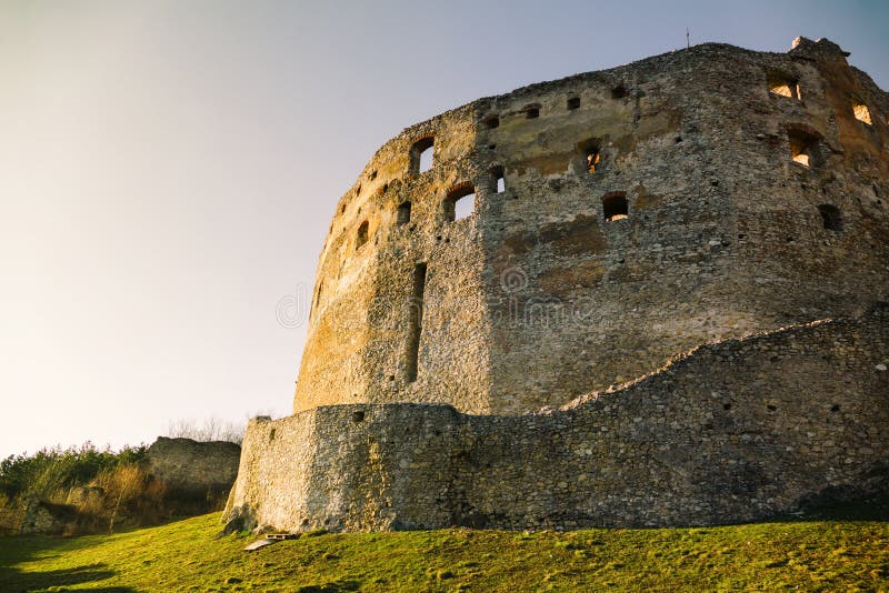 Ruiny hradu pri západe slnka so slnečnými lúčmi na vrchole. Osvetlený zámok na zelenej lúke s modrou oblohou