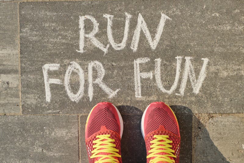 Run for fun, written on gray sidewalk with woman legs in sneakers, top view