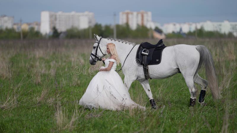 runaway bride and horse are walking on field, romantic woman and white equine