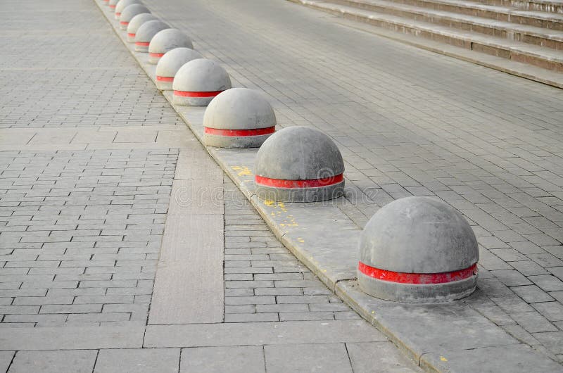 Round stone road kerb with a red strip standing in a row and on a diagonal on a paving stone. Round stone road kerb with a red strip standing in a row and on a diagonal on a paving stone.