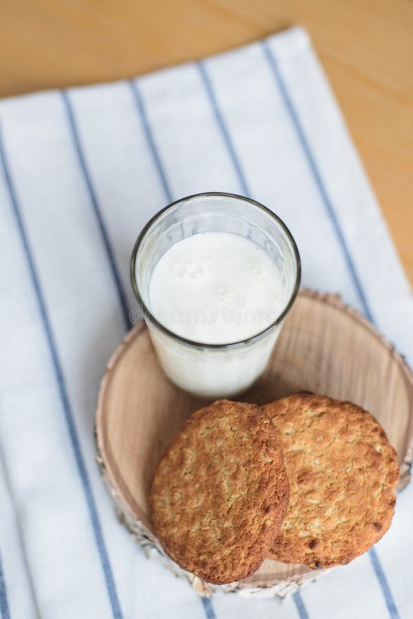 Runde braune Vollkornmehlplätzchen und Milchglas auf gestreifter weißer Serviette auf Holztisch stockbilder Runde braune Vollkornmehlplätzchen und Milchglas auf gestreifter weißer Serviette auf Holztisch stockbilder