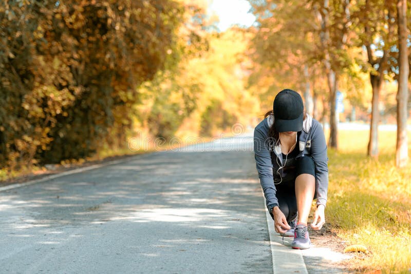 Running asian woman tying laces of running shoes before jogging through the road in the workout nature autumn park. stock photography Running asian woman tying laces of running shoes before jogging through the road in the workout nature autumn park. stock photography