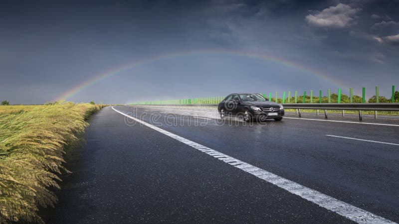 Running car in a rush on a highway away in the rain and together with the rainbow