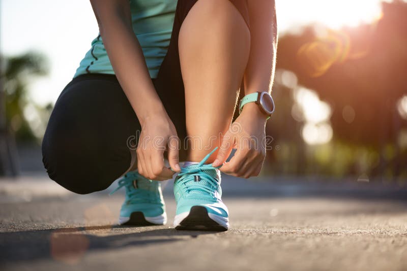 Running shoes - closeup of woman tying shoe laces. Female sport fitness runner getting ready for jogging in garden background.