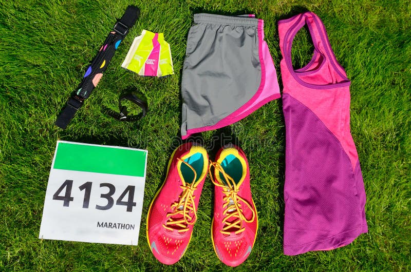 Running shoes, marathon race bib number, runners gear and energy gels on grass background, sport, fitness