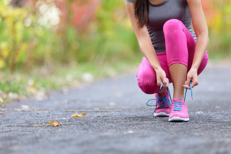 Running shoes woman runner tying shoe lace for run. Closeup of girl getting ready for jogging lacing sport shoe laces. Female sport fitness runner outdoors on forest path in spring fall season.