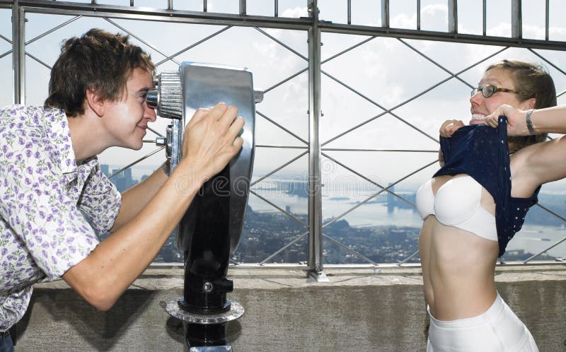 Young man looking at young woman through telescope as she lifts her top and shows her bra. Horizontal shot. Young man looking at young woman through telescope as she lifts her top and shows her bra. Horizontal shot.