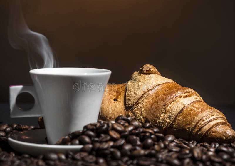 Coffee in a white cup and croissant on coffee beans background for stress in a business break. Coffee in a white cup and croissant on coffee beans background for stress in a business break