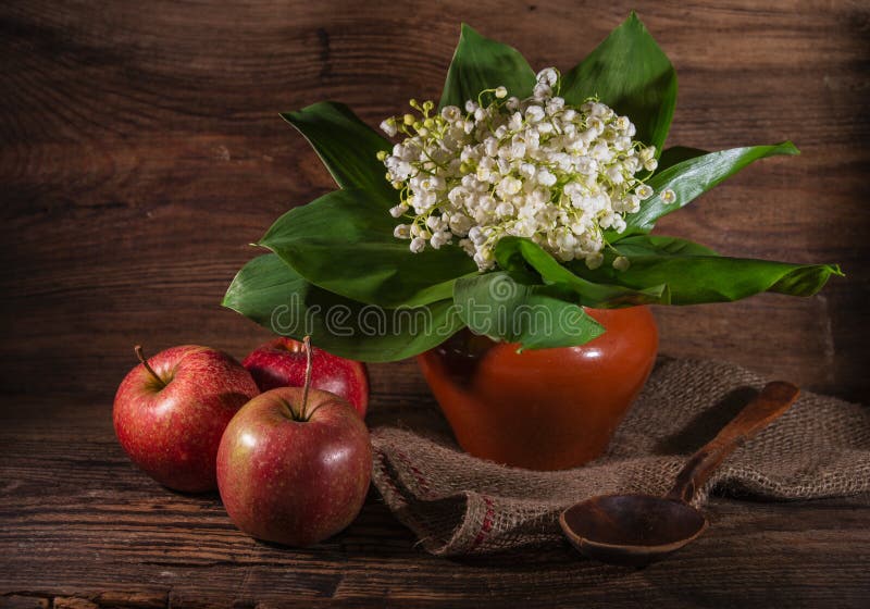 Rural still life with lilies of the valley and apples on wooden background