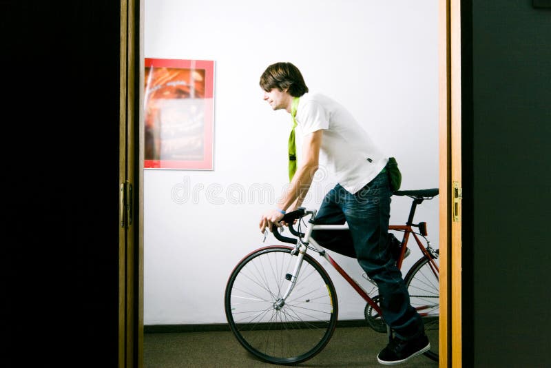 Giovane impiegato in sella al lavoro in bici attraverso l'ufficio sala all'ora di punta del mattino.