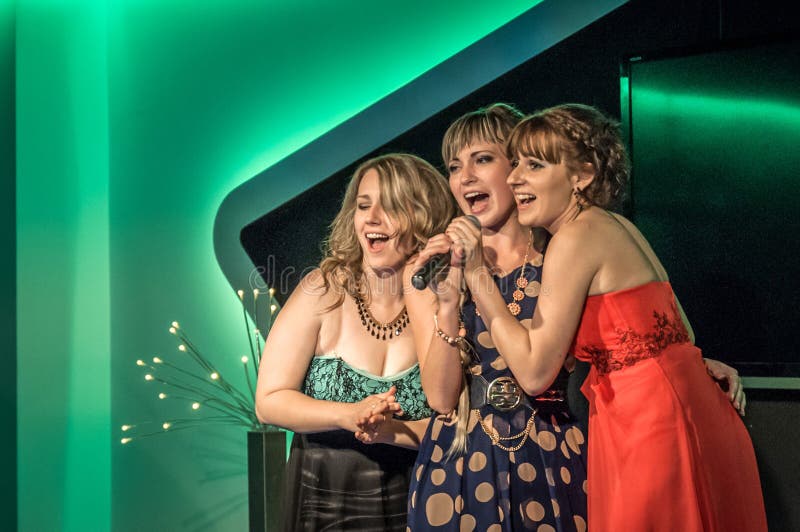 Rusia, Ryazan - 30 06 2014: tres muchachas hermosas que se colocan con el micrófono que canta apasionado con los ojos cerrados imagenes de archivo Rusia, Ryazan - 30 06 2014: tres muchachas hermosas que se colocan con el micrófono que canta apasionado con los ojos cerrados imagenes de archivo