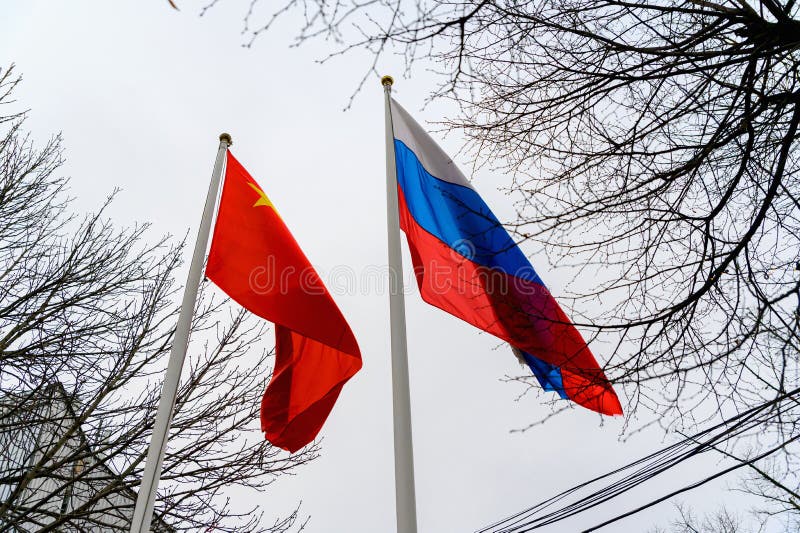 Russian and Chinese flags are flying in the wind. Flags of Russia and China on flagpoles