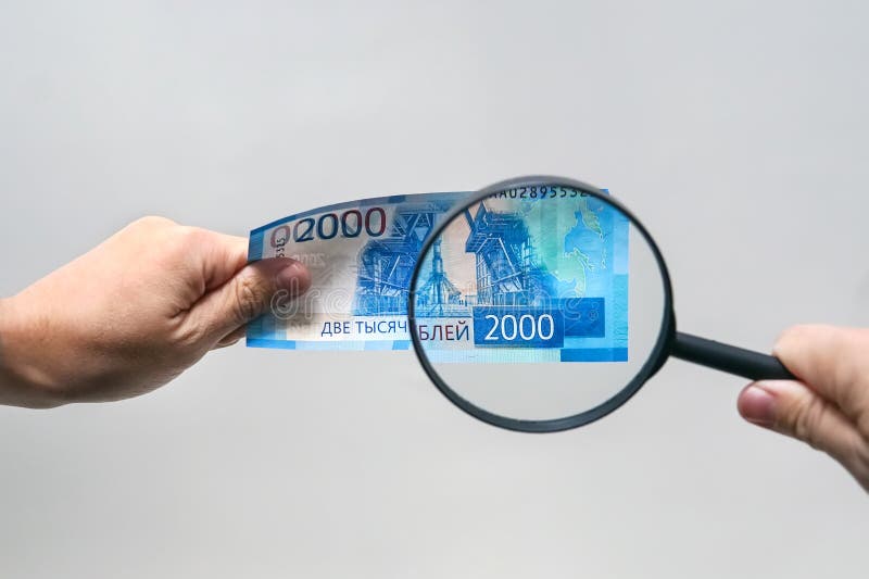 Russian currency, including new 2000 rouble bills. men's hands hold 2000 rubles and a magnifying glass. verification of the authe royalty free stock photo Russian currency, including new 2000 rouble bills. men's hands hold 2000 rubles and a magnifying glass. verification of the authe royalty free stock photo