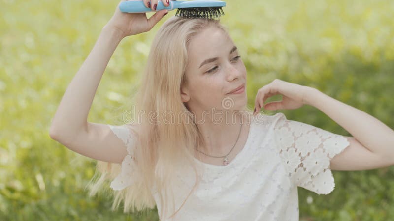 Russisches junges blondes Mädchen ist gekämmtes Sitzen auf dem Gras im Park