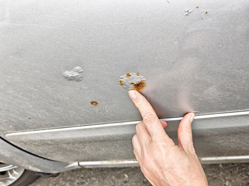 Rust spots on car surface are pointed out by a hand in a suburban driveway royalty free stock photography