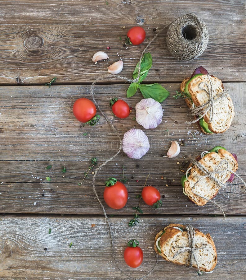 Rustic breakfast set. Sandwiches with smoked meat, cherry-tomatoes, cucumbers, garlic, thyme and basil on rough wood background