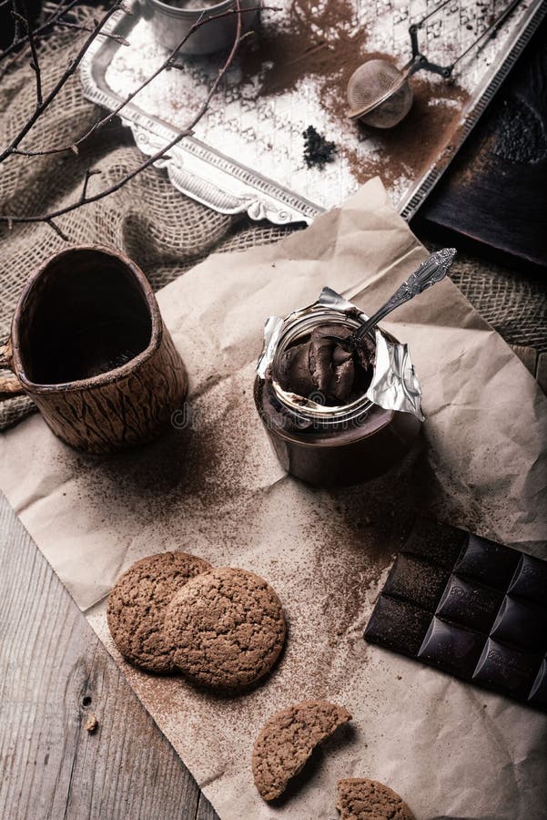 Rustic, dark and blurry background. grain. On the table is a jar of chocolate nut paste, a mug and oatmeal cookies stock images