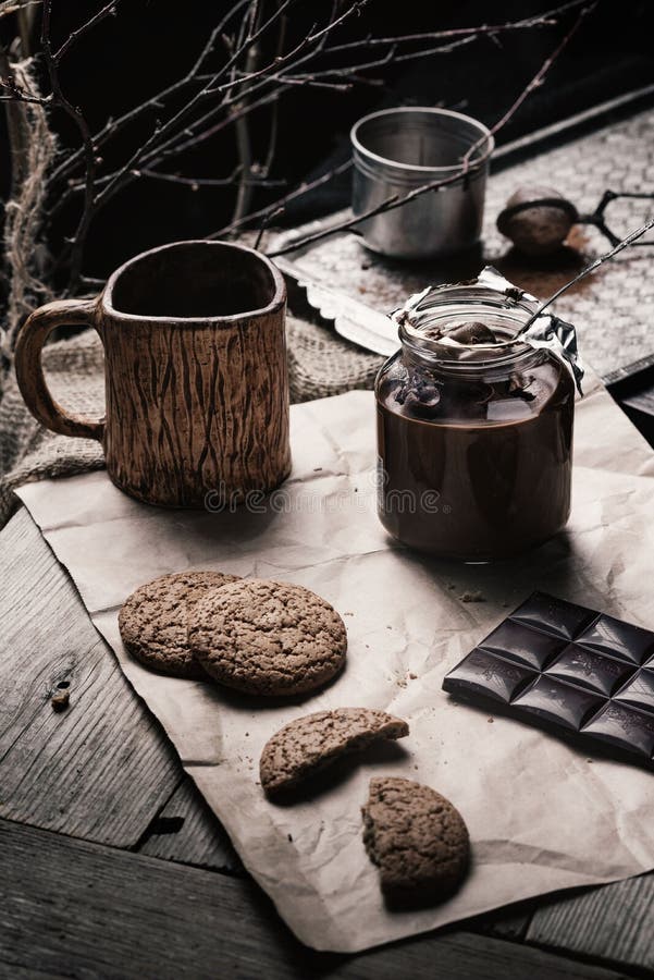 Rustic, dark and blurry background. grain. On the table is a jar of chocolate nut paste, a mug and oatmeal cookies stock photos