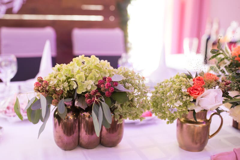 Rustic flower arrangement in a golden vase at a wedding banquet.