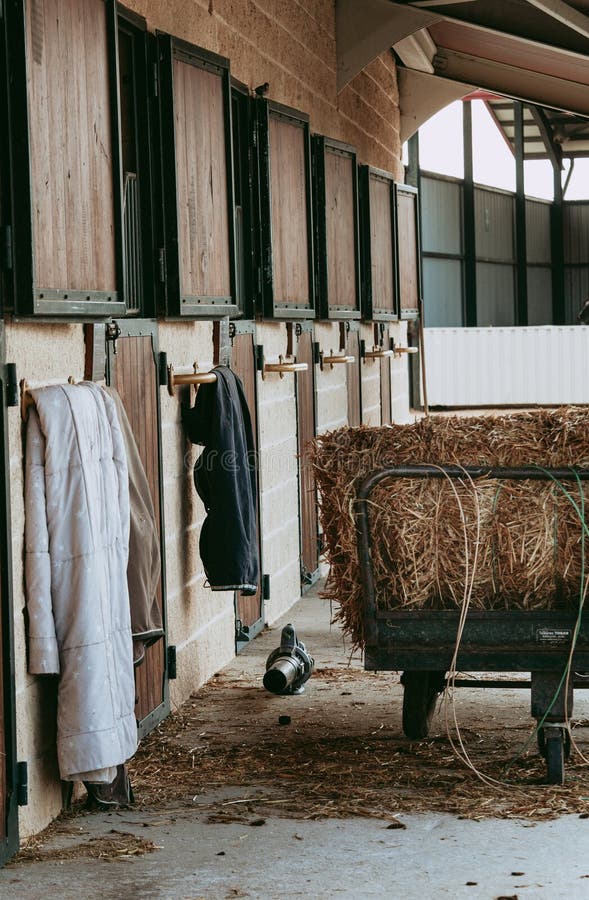 View of a rustic horse stable featuring hanging jackets and a bale of straw, evoking a serene and functional equestrian atmosphere. Stable rustic style stock images, royalty-free photos and pictures