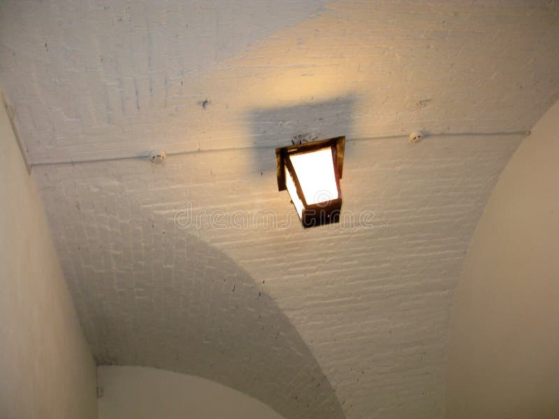 A rustic lantern hanging from a curved brick ceiling, casting a soft glow and subtle shadows in a historical interior space royalty free stock photo