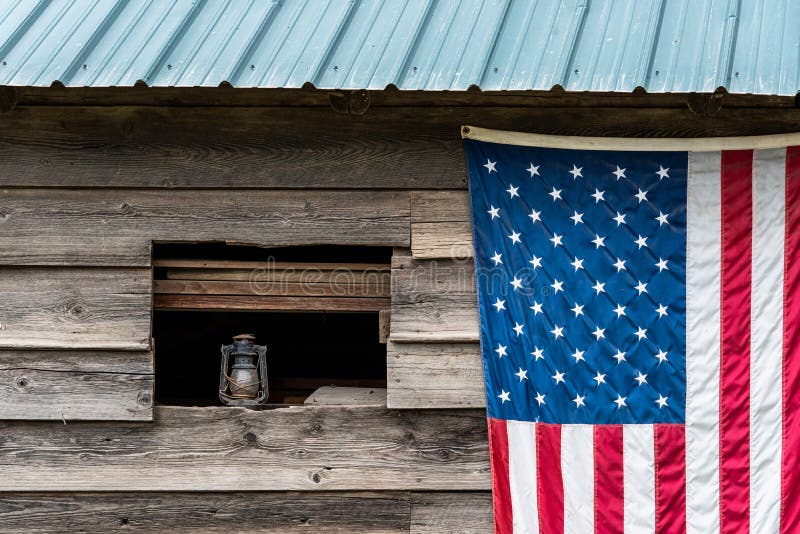 Rustic outside wall of wood building with green metal roof, open window with dusty lantern on windowsill, American flag hanging on stock photos Rustic outside wall of wood building with green metal roof, open window with dusty lantern on windowsill, American flag hanging on stock photos