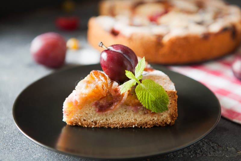 Homemade summer plum cake garnished with gooseberry and mint on dark background. Homemade summer plum cake garnished with gooseberry and mint on dark background