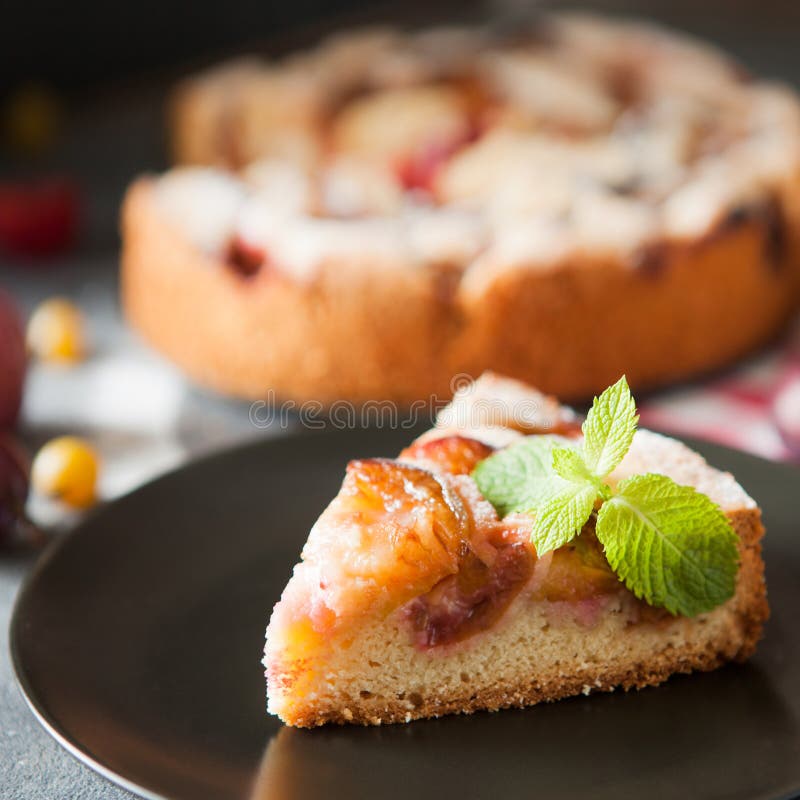 Homemade summer plum cake garnished with gooseberry and mint on dark background. Homemade summer plum cake garnished with gooseberry and mint on dark background