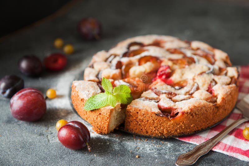 Homemade summer plum cake garnished with gooseberry and mint on dark background. Homemade summer plum cake garnished with gooseberry and mint on dark background