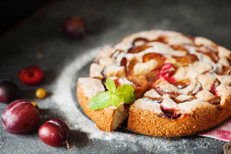 Homemade summer plum cake garnished with gooseberry and mint on dark background. Homemade summer plum cake garnished with gooseberry and mint on dark background